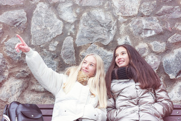 two young girls traveler look at the sights while sitting on a bench, stone wall background, travel and vacation concept