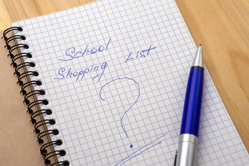 Blue pen on a notebook with sheets in a cage. Sign shopping list and question mark