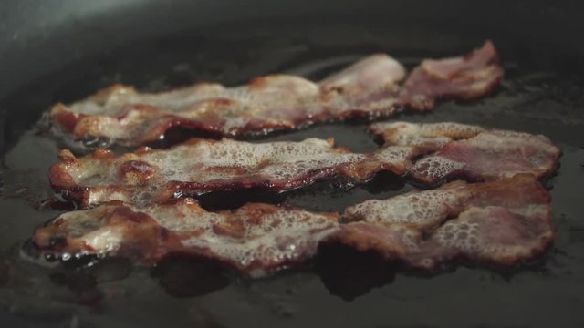 Crispy bacon strips fry in greasy fat in skillet, Slow Motion Close Up