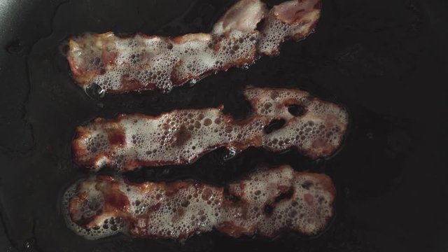 Overhead Close Up, Bacon strips sizzle in skillet in Slow Motion