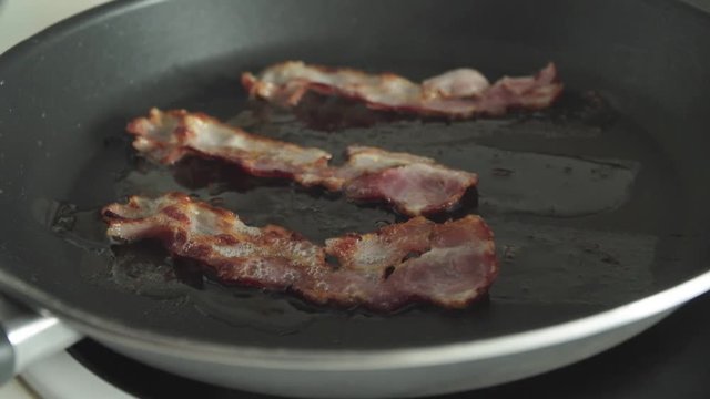 Flipping bacon strip in frying pan, Slow Motion Close Up