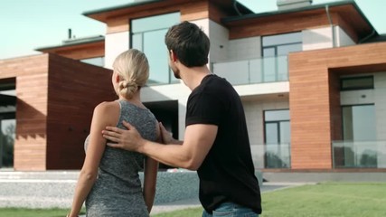 Handsome man closing woman eyes near house. Surprised woman standing near villa