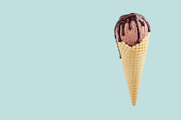 Brown ice cream in crisp waffle cone with chocolate sauce on pastel green background, mock up for design.