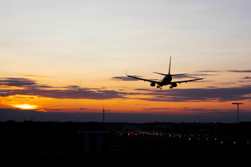 Fototapeta na wymiar Plane over the landing strip at gold sunset. Cloudy purple sky background.