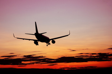 Silhouette of plane flying at red sunset. Cloudy purple sky background.