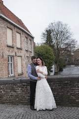 Wedding photo shooting. Bride and bridegroom walking in Brugge. Stand on bridge and hug.