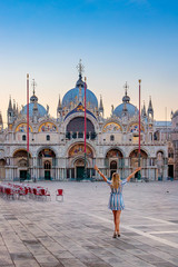 Woman enjoying the view of San Marco Cathedral in Venice, Italy. A slender woman with her hands up. Sunrise on St. Mark's square.