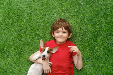 Child embracing puppy jack russell and lying on green carpet.