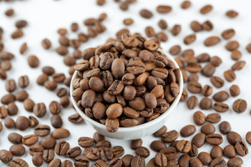 Roasted coffee beans in ceramic bowl on white, close-up