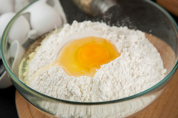 Wheat flour with egg in glass bowl on wooden cutting board