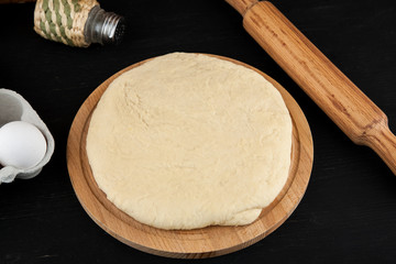Raw fresh dough on wooden cutting board on black table, pizza cooking process