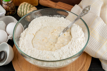 Making dough for pizza, flour with spoon in glass bowl on wooden cutting board