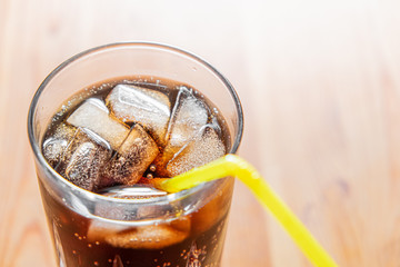 Icy cold beverage in a glass, close-up view. Glass of cool fizzy drink with ice on a wood table, point of view shot