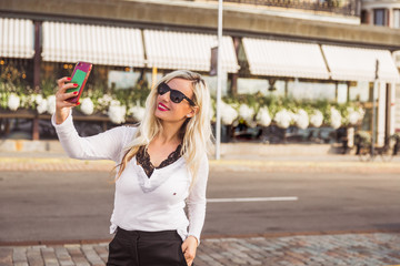 Naklejka premium Portrait of the cheerful young woman who is standing on the street and doing selfie photo