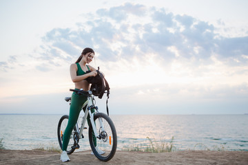 Portrait of a beautiful young brunette woman with a backpack resting after bicycle ride at sunrise.