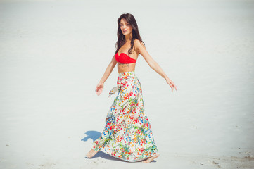 A beautiful woman dressed in beach clothes gracefully walks in the desert in the sand