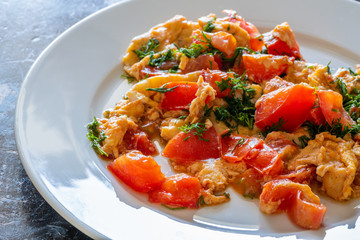 Scrambled eggs with tomato and dill on a white plate 
