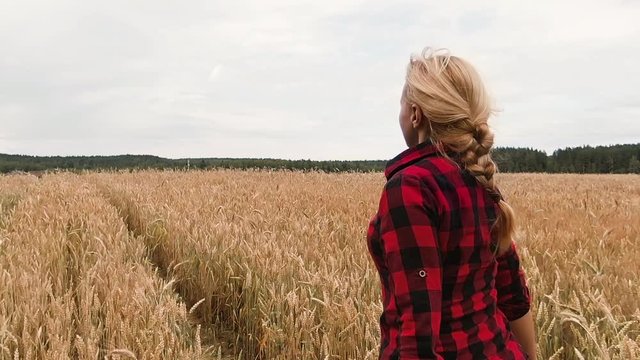 Young girl in a red checkered shirt runs through a ripe wheat field. Slow motion. Girl farmer happy harvest. Enjoyment of freedom, happiness, life.