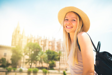 Summer hot vacation Europe Spain holiday travel tourism architecture - young beautiful Caucasian walking smiling attractive young girl with hat and backpack in front of the city castle in the city