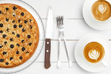 Two cups of coffee and homemade pie with cottage cheese souffle decorated with almonds and blueberries on white wooden table. Top view.