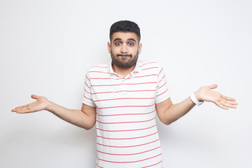 I don't know. Portrait of confused handsome bearded young man in striped t-shirt standing with raised arms and dont know what to do. indoor studio shot, isolated on white background.