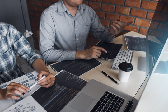 Two software developers are using computers to work together with their partner at the office desk.