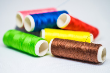 Multi-colored spools of cotton threads for sewing on a white background close-up