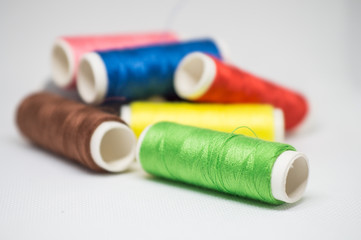 Multi-colored spools of cotton threads for sewing on a white background close-up
