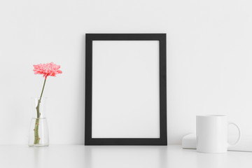 Black frame mockup with a chrysanthemum in a vase, book and a mug on a white table. Portrait...