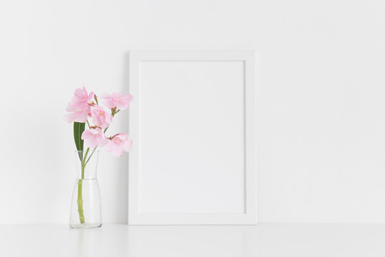 White frame mockup with pink oleander in a glass vase on a white table.Portrait orientation.
