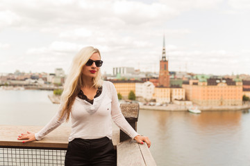 Portrait of the beautiful young woman who is standing against the background of the city and river