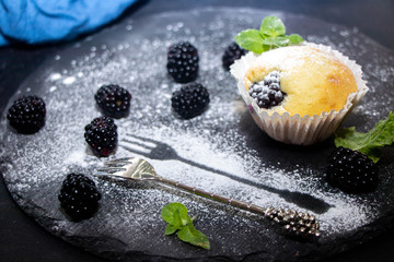On a black background the muffin is covered with powdered sugar, a metal fork is lying next to it and the decor is made with powdered sugar. 