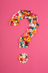 Question mark arranged from assorted pharmaceutical medicine pills, tablets and capsules on pink background