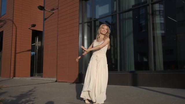 cute girl in a long dress dancing against the backdrop of a modern building