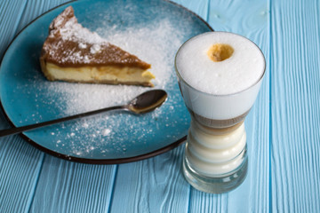 The cheesecake in a plate and latte on a blue wooden table.