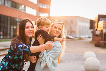 Portrait of the two young women who are standing with the little boy outdoor and looking at something