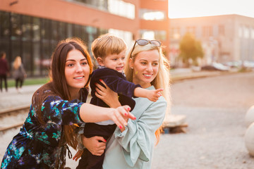 Portrait of the two smiling young women who are standing with the little boy outdoor and looking at something