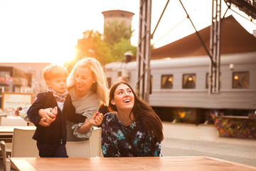 Two cheerful young women sitting on the station with the cute little boy