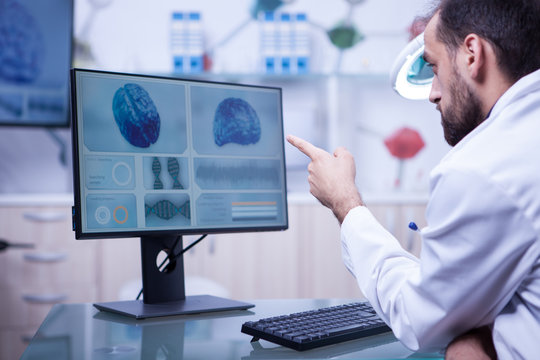 Bearded doctor in white coat pointing at a brain x-ray on the monitor