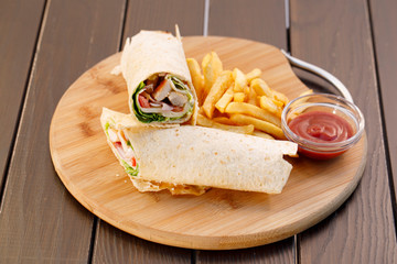 Wrapped sandwich chicken tortilla with fried potatoes and dipping sauce on wooden plate , wood background.
