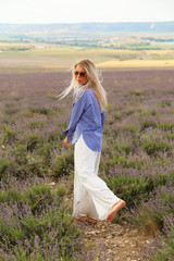 Fototapeta na wymiar beautiful woman with blond hair in elegant clothes and accessories posing in flowering lavender field