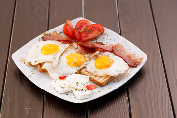 Healthy bacon fried egg on toast bread breakfast on plate , fresh tomatoes and cheese on plate , wood background.