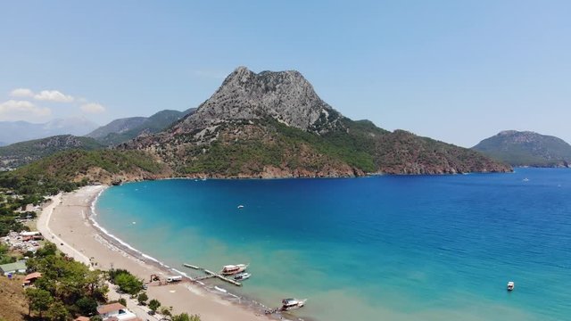 An aerial view of Adrasan beach in Turkey and a small mountain peak meeting the blue water in the background on a sunny summer day