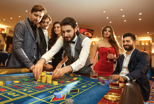 A young man with friends makes bets on roulette in a casino.