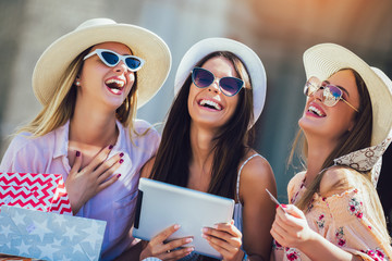 Three girls with colorful shopping bags using digital tablet and credit card