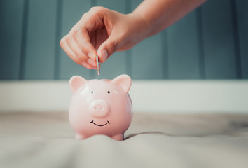 Woman Hand is Putting a Money Coin into Piggy Bank for Savings on The Bedroom., Female Hand is Inserting Coin in Pink Piggybank., Saving for The Finance Future, Business Banking and Financial Concept.