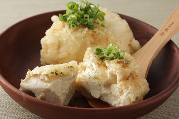 薄緑の背景に木の器に載せた揚げ出し豆腐