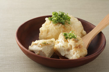 薄緑の背景に木の器に載せた揚げ出し豆腐