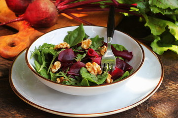 Healthy Beet Salad with fresh sweet baby spinach, arugula, nuts on wooden background