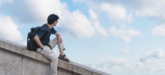 Asian man with backpack looking at blue sky and white clouds in summer